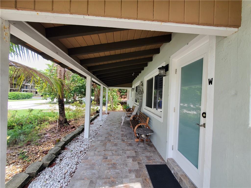 A covered porch with tiled flooring, wooden benches, and a white door with a window — 3204 NE 6th Street, Pompano Beach FL 33062, POMPANO BEACH, FL