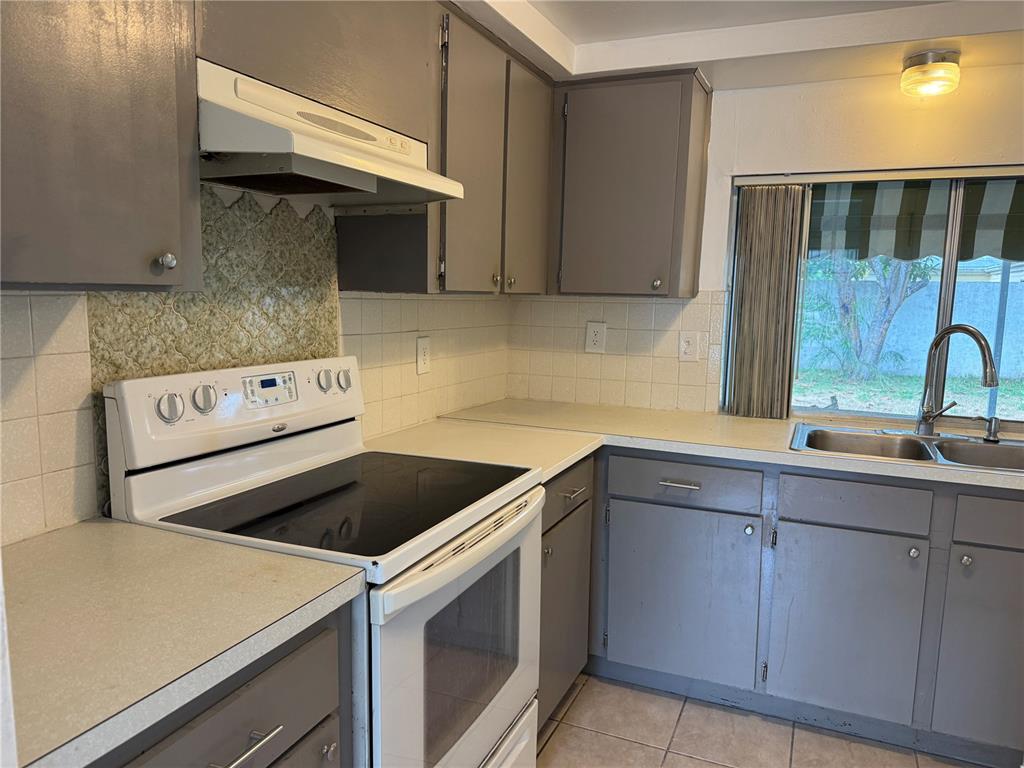 A kitchen features gray cabinets, white appliances, a tiled backsplash, and a window above the sink — 12411 PARTRIDGE HILL ROW, HUDSON, FL