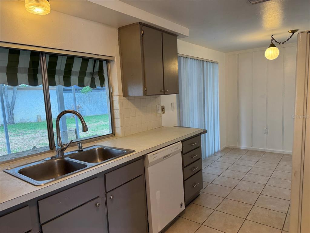 A kitchen features gray cabinets, a double sink, a white dishwasher, and tiled flooring — 12411 PARTRIDGE HILL ROW, HUDSON, FL