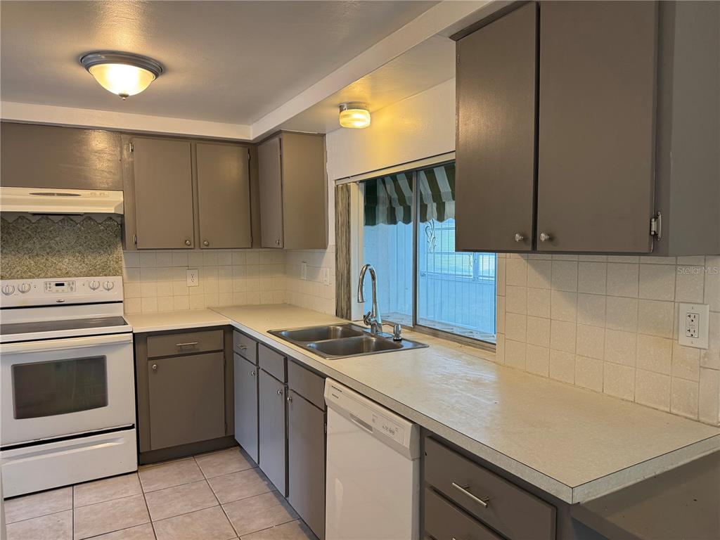 A kitchen features gray cabinets, white appliances, tiled countertops, and a window above the sink — 12411 PARTRIDGE HILL ROW, HUDSON, FL