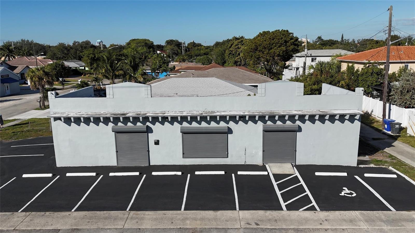 An exterior view of a single-story commercial building with three roll-down doors and parking — 3000 N 22nd Avenue, Hollywood FL 33020, HOLLYWOOD, FL