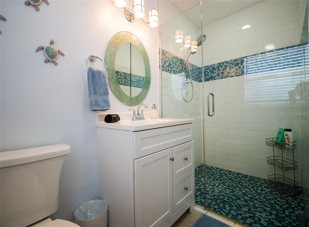 A bathroom features a white vanity, a round mirror, and a glass-enclosed shower with tile — 1312 66TH STREET NW, BRADENTON, FL