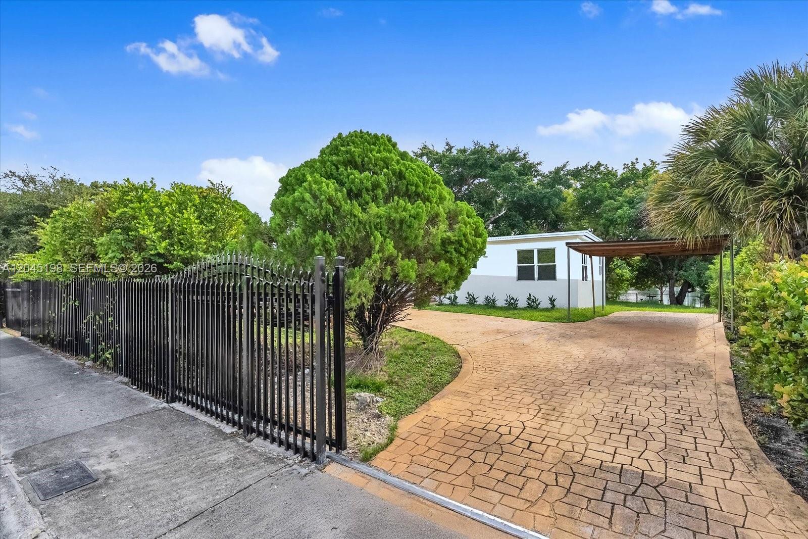 A paved driveway leads to a small house behind a black metal fence — 13415 NW 22nd Ave, Miami FL 33167, MIAMI, FL