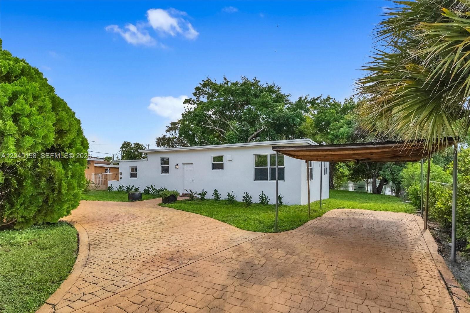 A white single-story house features a paved driveway, a carport, and surrounding green landscaping — 13415 NW 22nd Ave, Miami FL 33167, MIAMI, FL