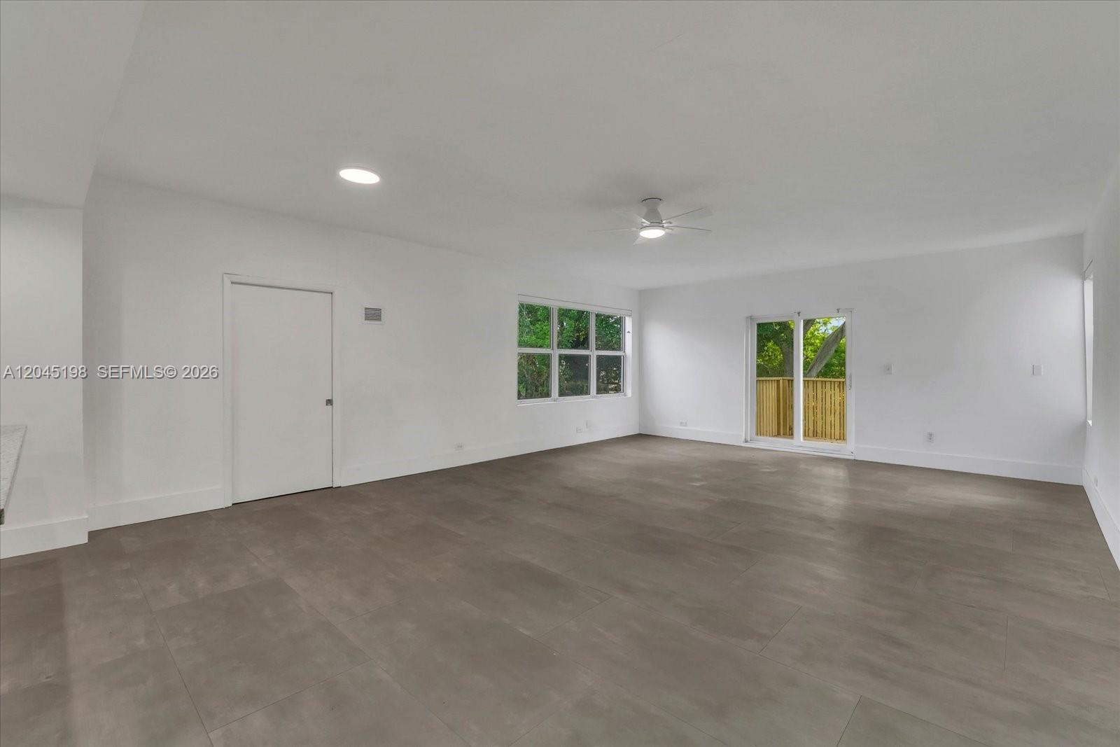 A spacious, empty room features white walls, gray tile flooring, a ceiling fan, and sliding doors — 13415 NW 22nd Ave, Miami FL 33167, MIAMI, FL