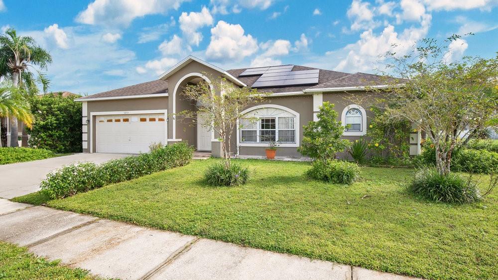 A single-story house with a tan exterior, a two-car garage, and solar panels on the roof — 5203 JASMINE TRACE LANE, KISSIMMEE, FL