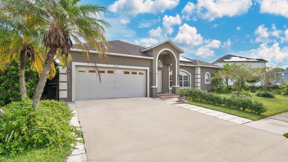 A single-story house with a two-car garage, a palm tree, and a concrete driveway — 5203 JASMINE TRACE LANE, KISSIMMEE, FL