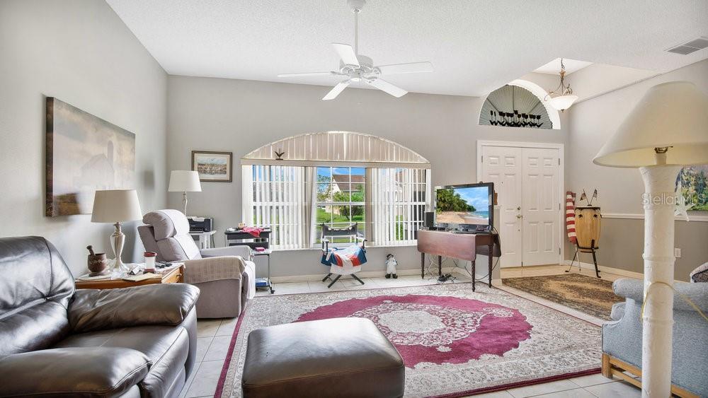 A living room features a vaulted ceiling, a ceiling fan, a large rug, and windows — 5203 JASMINE TRACE LANE, KISSIMMEE, FL