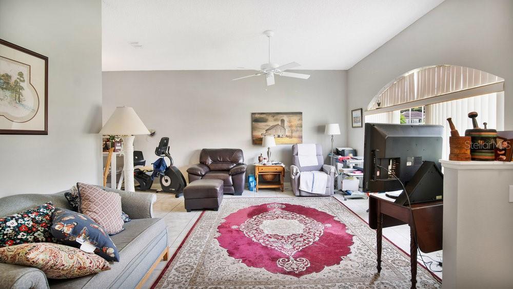 A living room features a large red area rug, a sofa, armchairs, and exercise equipment — 5203 JASMINE TRACE LANE, KISSIMMEE, FL
