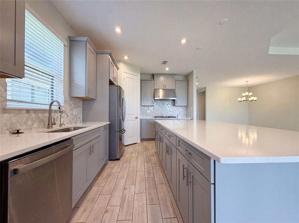 A modern kitchen features gray cabinets, white countertops, a large island, and wood-look tile flooring — 4516 CRESTPOINT WAY, PALMETTO, FL