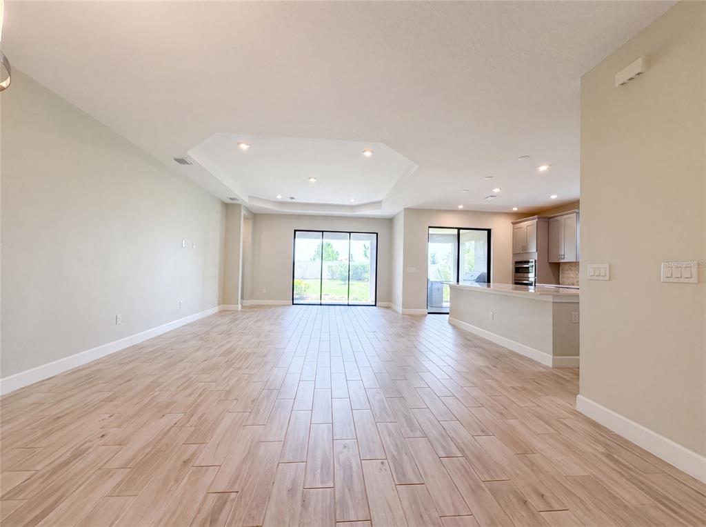 An open-concept living area features light wood-look tile flooring, a tray ceiling, and a kitchen — 4516 CRESTPOINT WAY, PALMETTO, FL