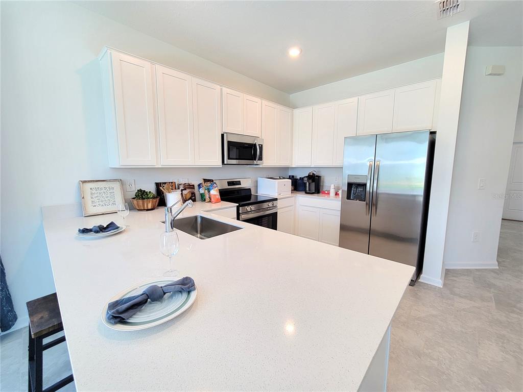 A modern kitchen features white cabinets, stainless steel appliances, and a large quartz island — 2881 PIERR STREET, DAVENPORT, FL