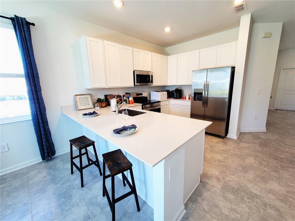 A kitchen features white cabinets, stainless steel appliances, a quartz island, and two wooden stools — 2881 PIERR STREET, DAVENPORT, FL