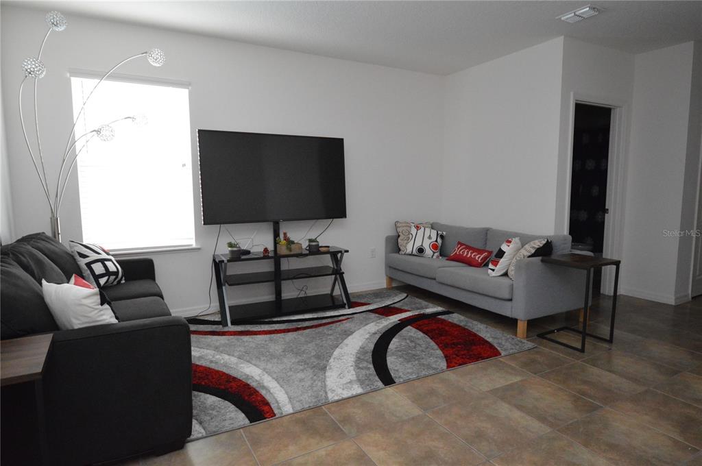A living room features a grey sofa, a black sofa, a patterned rug, and a television — 937 GILA PLACE, KISSIMMEE, FL