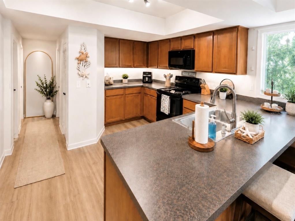 A kitchen with wood cabinets, dark countertops, a central island, and a hallway entrance — 6 MASTERS COURT UNIT 6, PALM COAST, FL