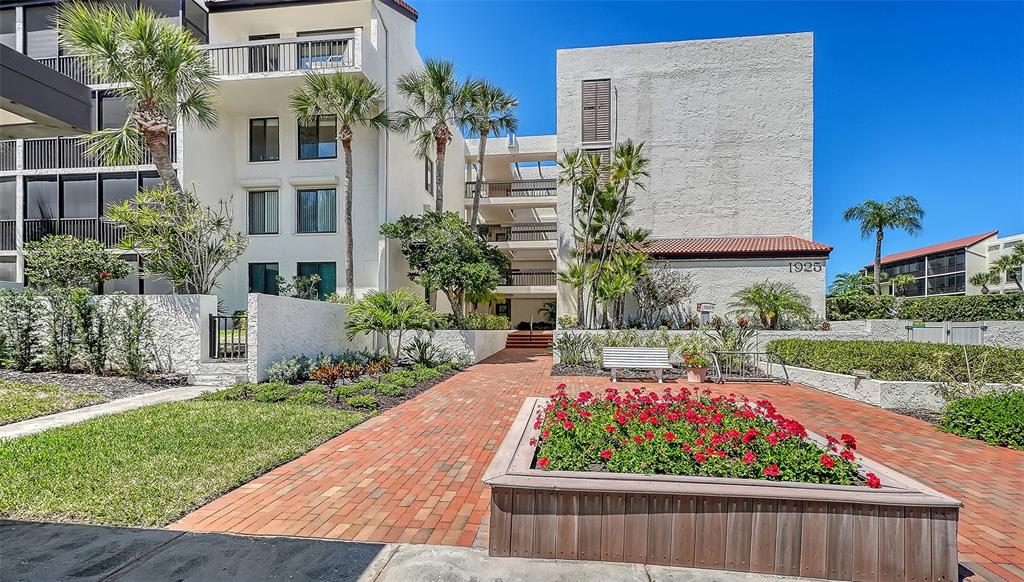 A brick walkway leads to the entrance of a multi-story apartment building with palm trees — 1925 GULF OF MEXICO DRIVE UNIT G8-302, LONGBOAT KEY, FL