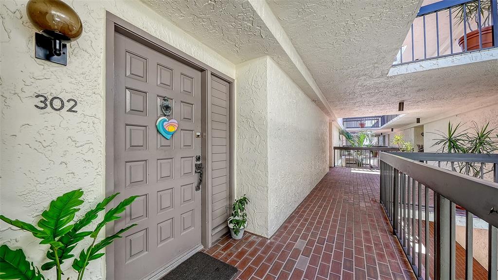 The exterior view shows a brown front door with a heart decoration and brick walkway — 1925 GULF OF MEXICO DRIVE UNIT G8-302, LONGBOAT KEY, FL