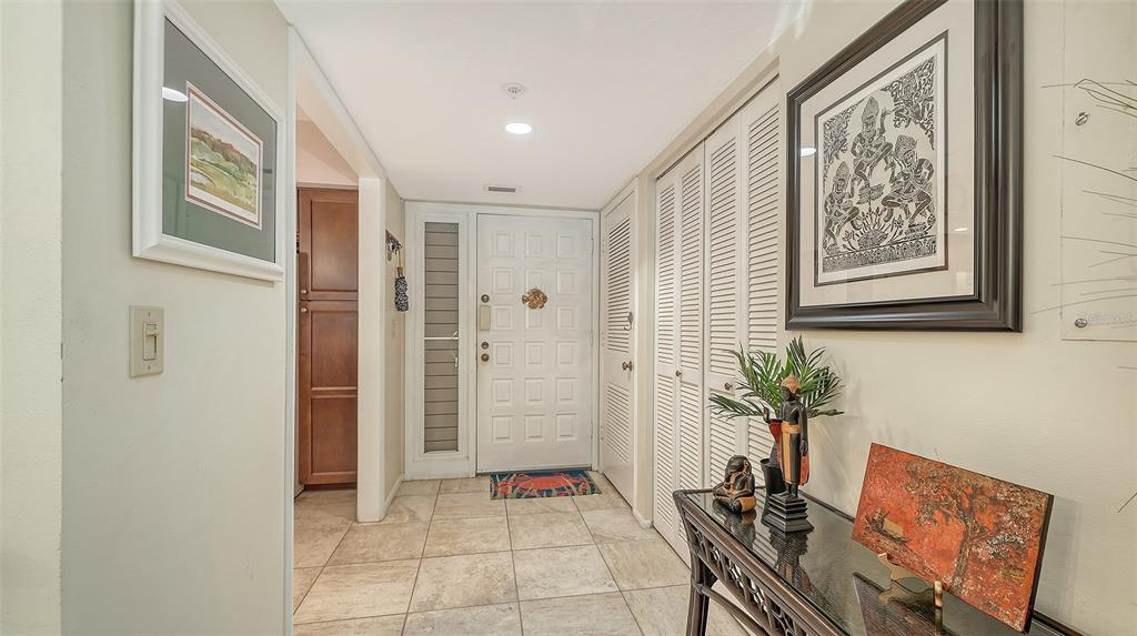 An entryway features tiled floors, a white paneled door, louvered closet doors, and framed artwork — 1925 GULF OF MEXICO DRIVE UNIT G8-302, LONGBOAT KEY, FL