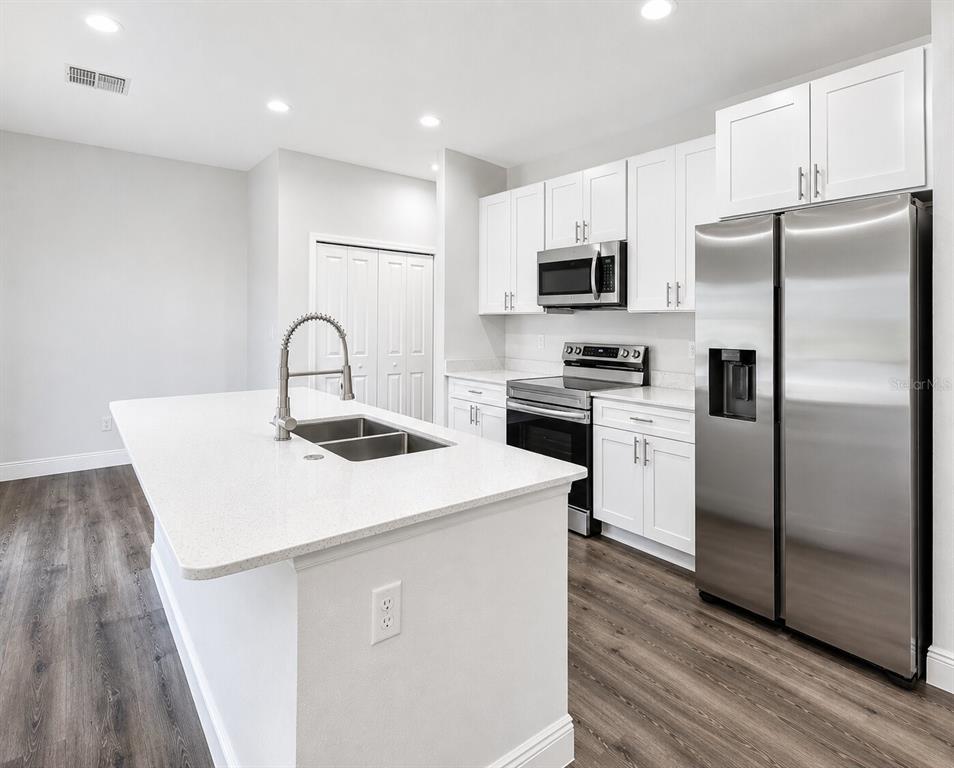 A modern kitchen features white cabinets, stainless steel appliances, a quartz island, and wood flooring — 39 WATER TRACK DRIVE, OCALA, FL