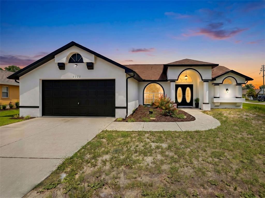 A single-story house with a black garage door, white stucco walls, and a arched entryway — 6170 GAINSBORO AVENUE, SPRING HILL, FL
