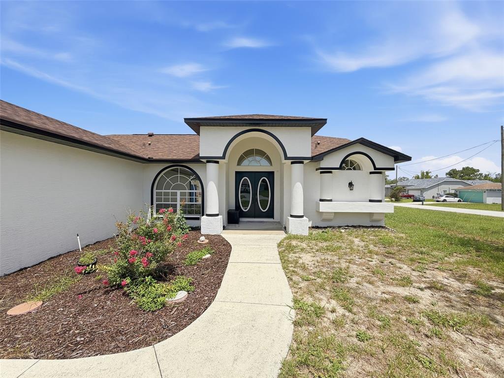 A single-story house with a white stucco exterior, arched entryway, and a concrete walkway — 6170 GAINSBORO AVENUE, SPRING HILL, FL