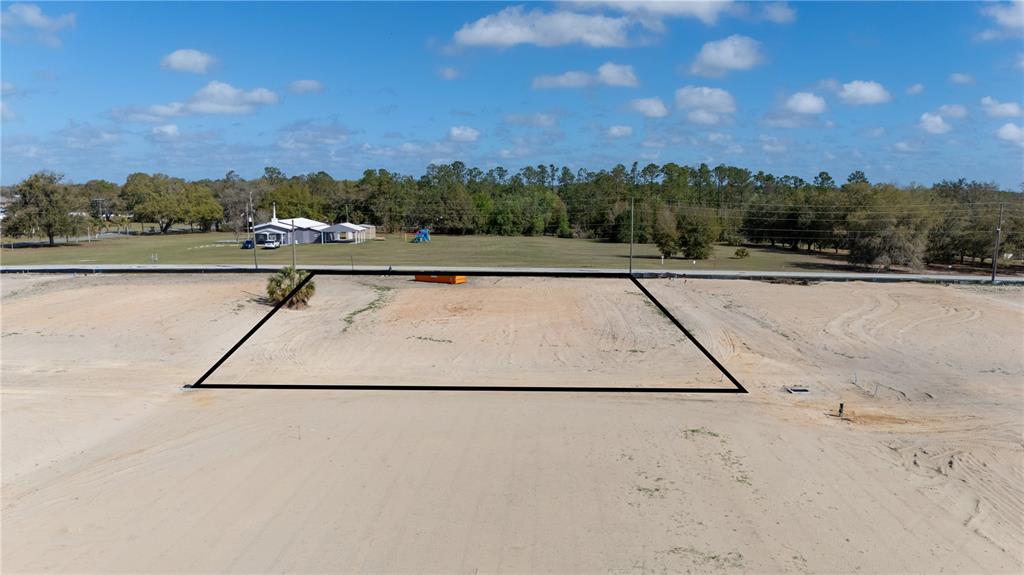 An aerial view shows a vacant, sandy rectangular lot outlined in black near a road — 32806 DUNNE ROAD, SAN ANTONIO, FL