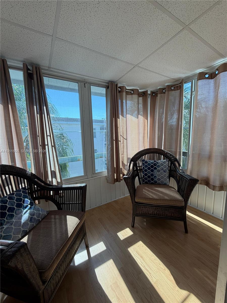 A sunroom features two wicker chairs, light wood flooring, and large windows with brown curtains — 1832 Sunny Drive # 32, Bradenton FL 34207, BRADENTON, FL