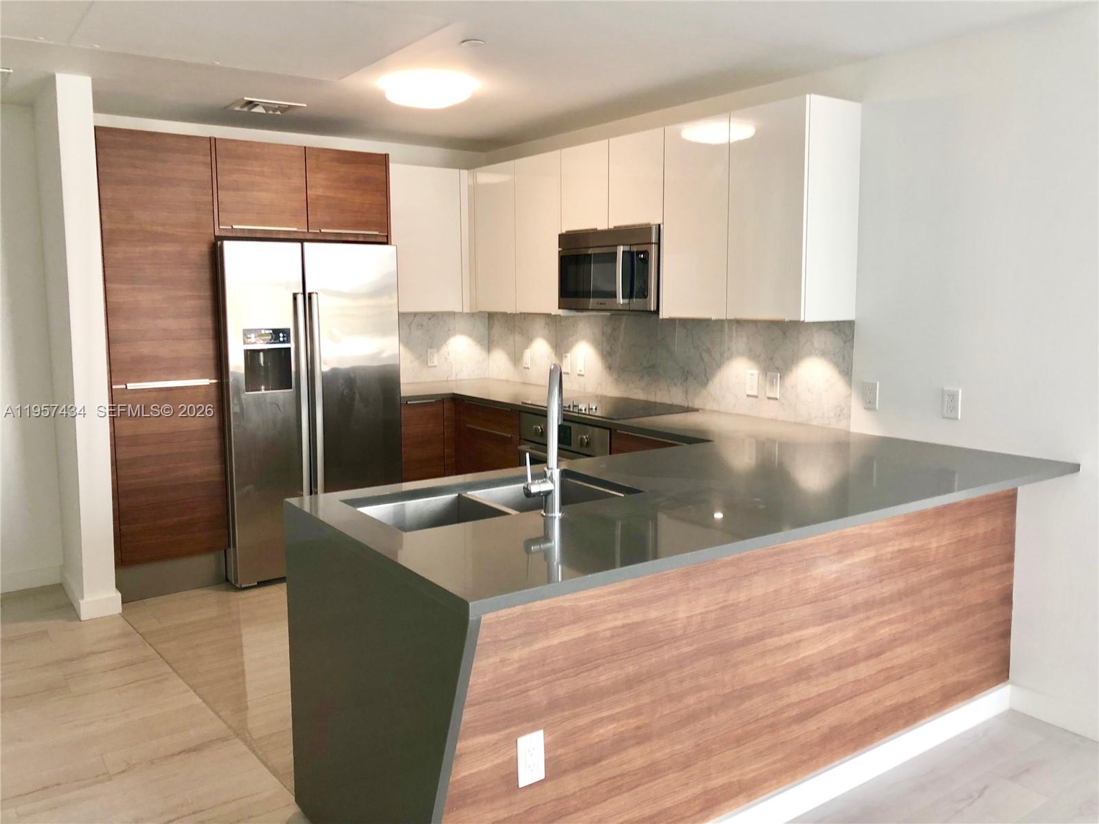 A modern kitchen features wood-tone and white cabinetry, stainless steel appliances, and a gray countertop — 601 NE 27TH ST # 801, Miami FL 33137, MIAMI, FL