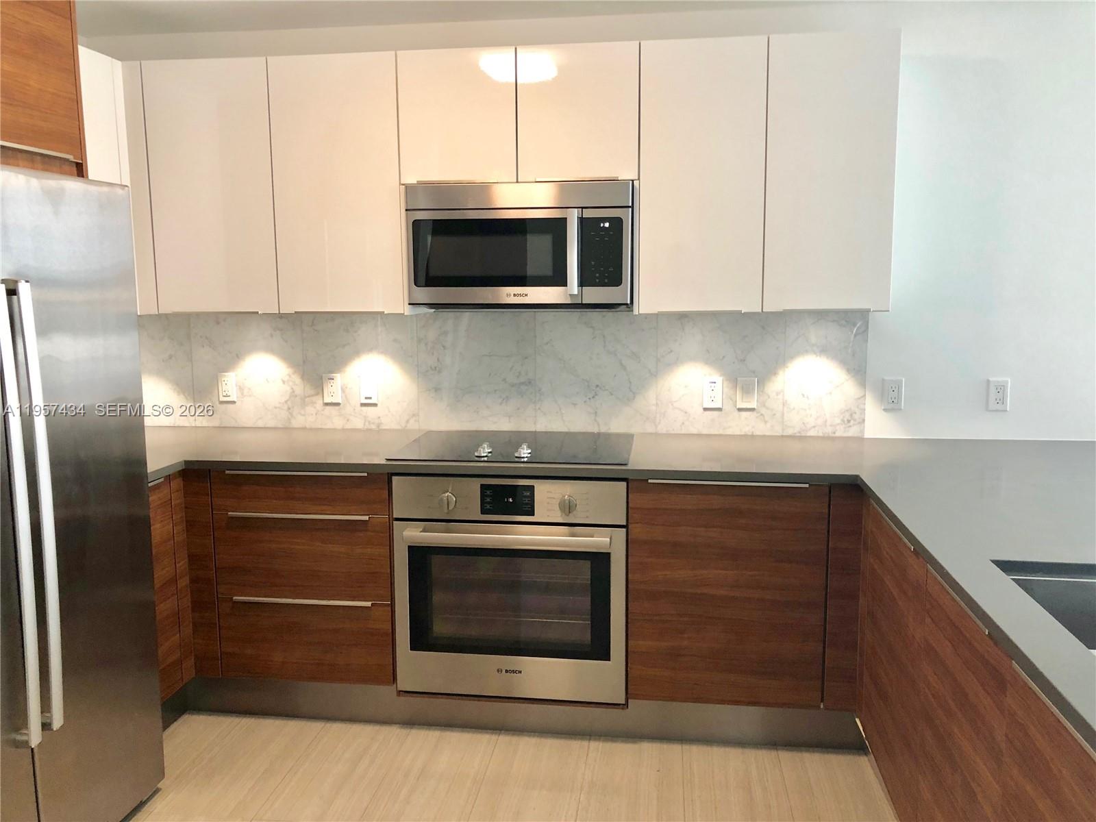 A modern kitchen features wood-grain lower cabinets, white upper cabinets, and stainless steel appliances — 601 NE 27TH ST # 801, Miami FL 33137, MIAMI, FL