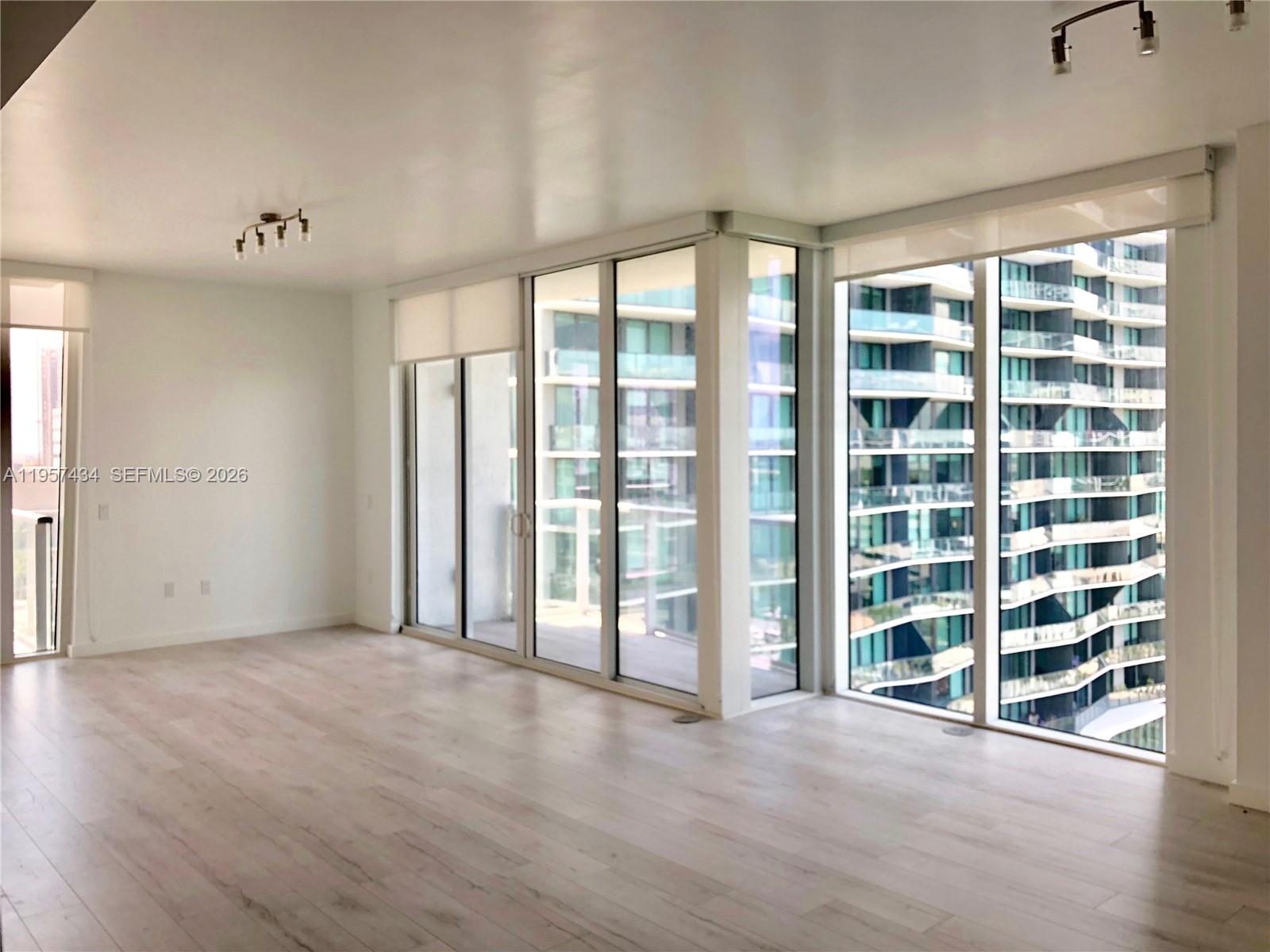 An empty room features light wood flooring, white walls, and floor-to-ceiling windows overlooking another building — 601 NE 27TH ST # 801, Miami FL 33137, MIAMI, FL