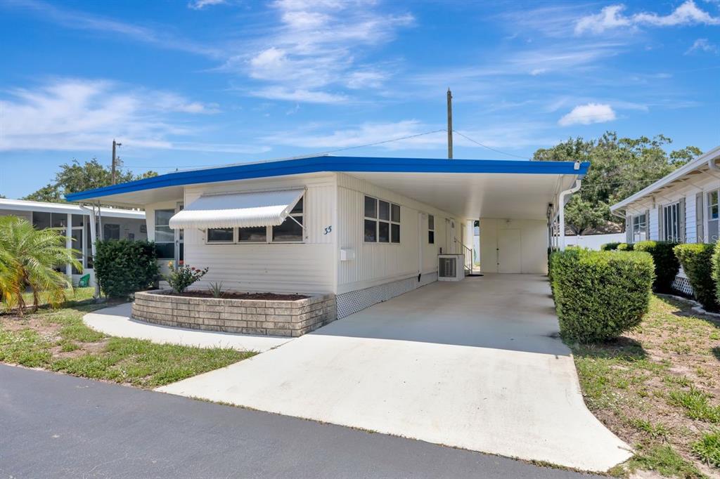 A single-story mobile home with a blue roof, white siding, and an attached carport — 9900 ULMERTON ROAD UNIT 35, LARGO, FL
