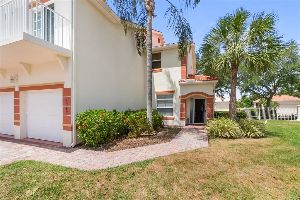 A two-story stucco townhouse features a garage, a brick walkway, and a palm tree — 7343 FOUNTAIN PALM CIRCLE UNIT na, BRADENTON, FL