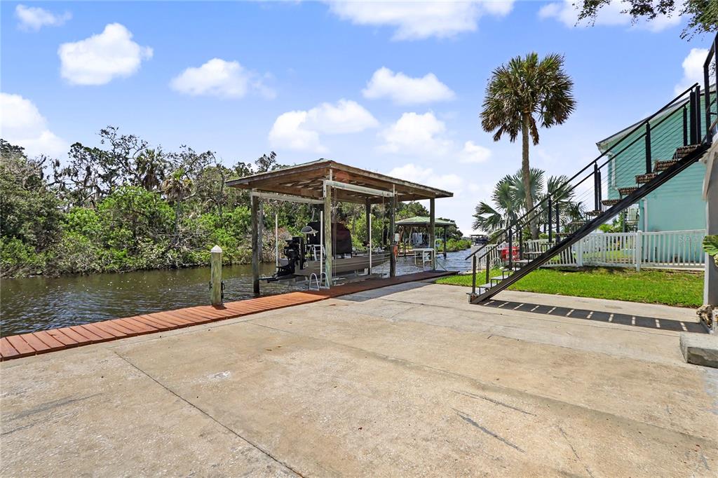 A concrete patio leads to a wooden boat dock with a covered slip on a canal — 12390 W STANDISH, HOMOSASSA, FL