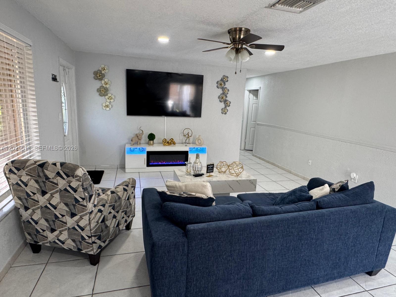 A living room features a blue sofa, patterned armchair, television, and an electric fireplace console — 5844-5846 Pierce St, Hollywood FL 33021, HOLLYWOOD, FL