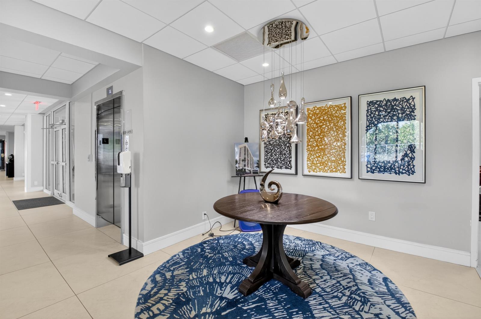 A lobby features a round wooden table, a blue patterned rug, and modern pendant lighting — 1180 S Ocean Boulevard # 5c, Boca Raton FL 33432, BOCA RATON, FL