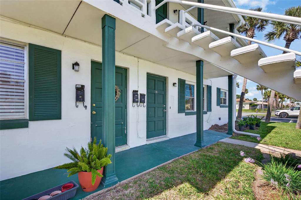 A ground-level exterior view of a building with green doors, shutters, and a staircase — 1800 S PALMETTO AVENUE UNIT 1010, SOUTH DAYTONA, FL
