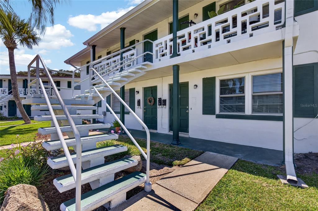 An exterior view of a two-story apartment building with white walls and green stairs — 1800 S PALMETTO AVENUE UNIT 1010, SOUTH DAYTONA, FL