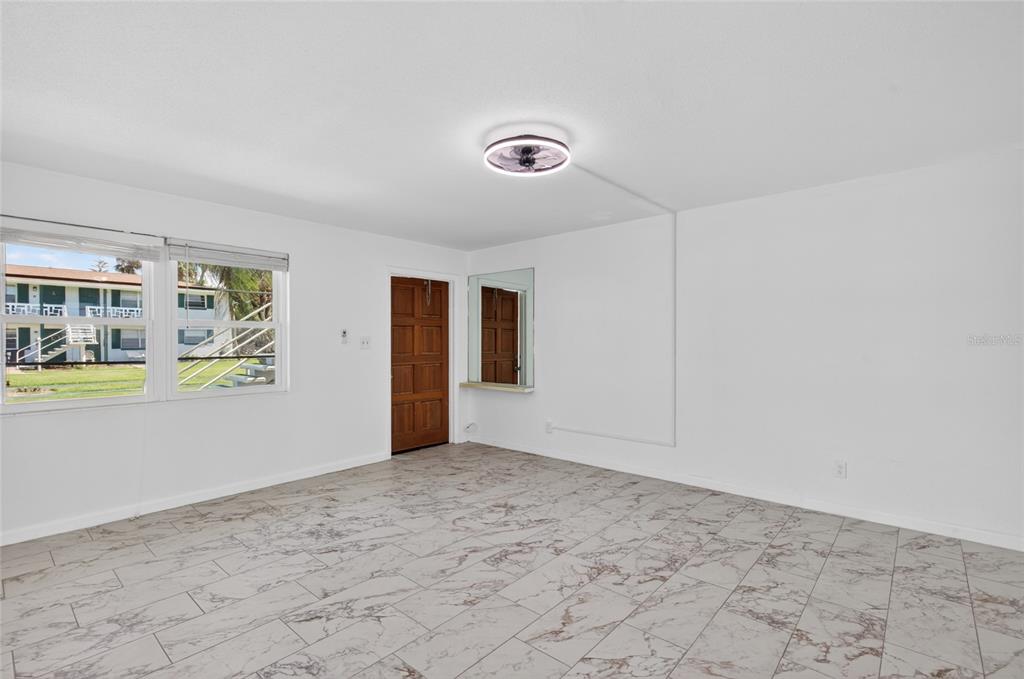 A bright room with white walls, tiled floors, a ceiling fan, and a wooden door — 1800 S PALMETTO AVENUE UNIT 1010, SOUTH DAYTONA, FL