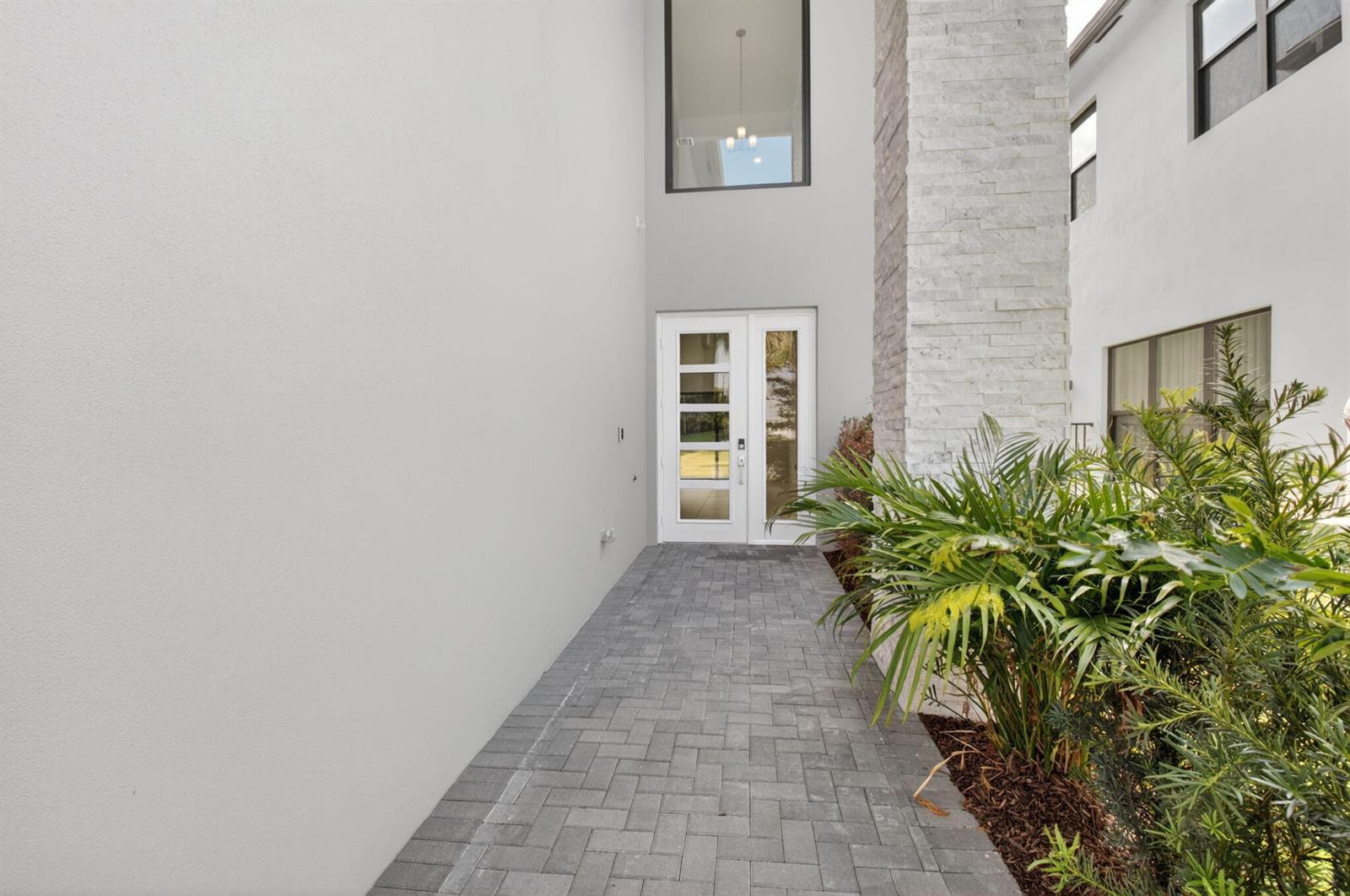 A paved walkway leads to a white front door beside a stone-clad exterior pillar — 21054 Violet Fields Way, Boca Raton FL 33434, BOCA RATON, FL