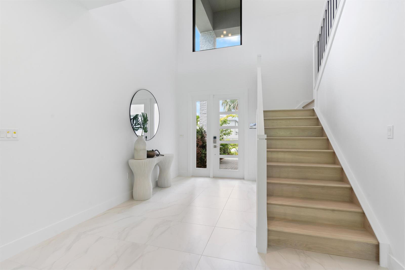 A bright entryway features white tile floors, a wooden staircase, and a modern console table — 21054 Violet Fields Way, Boca Raton FL 33434, BOCA RATON, FL