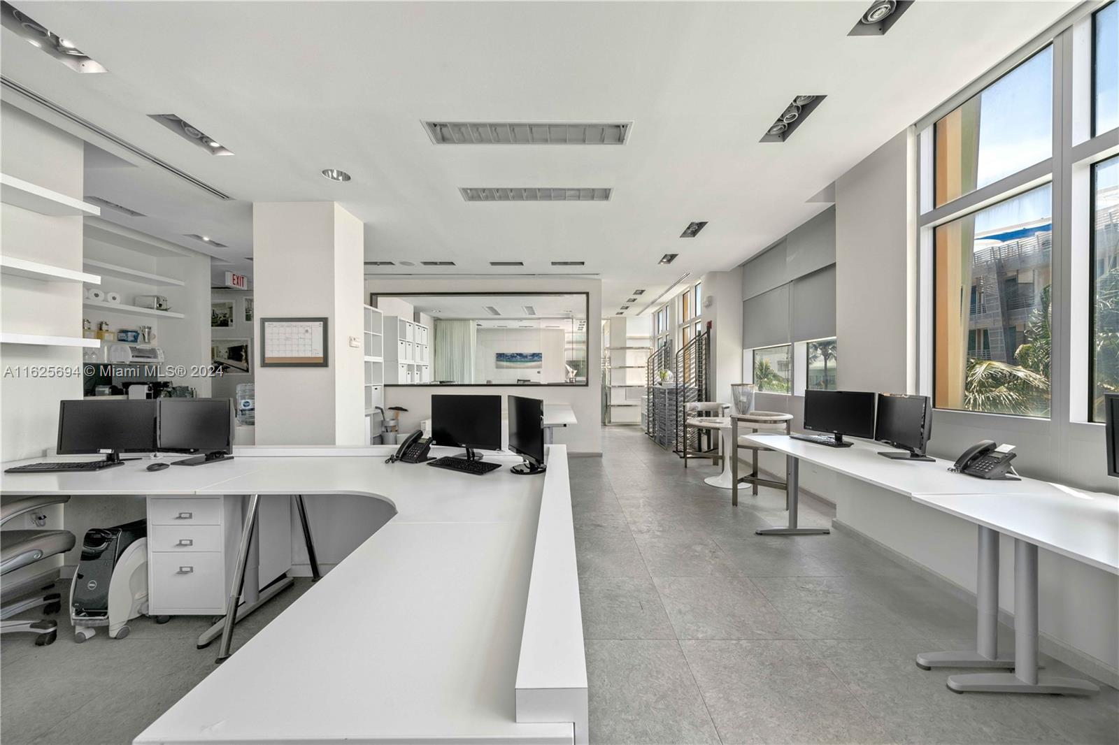 A bright office space features white desks, multiple computer monitors, and large windows with views — 1451 Ocean Dr # 204, Miami Beach FL 33139, MIAMI BEACH, FL