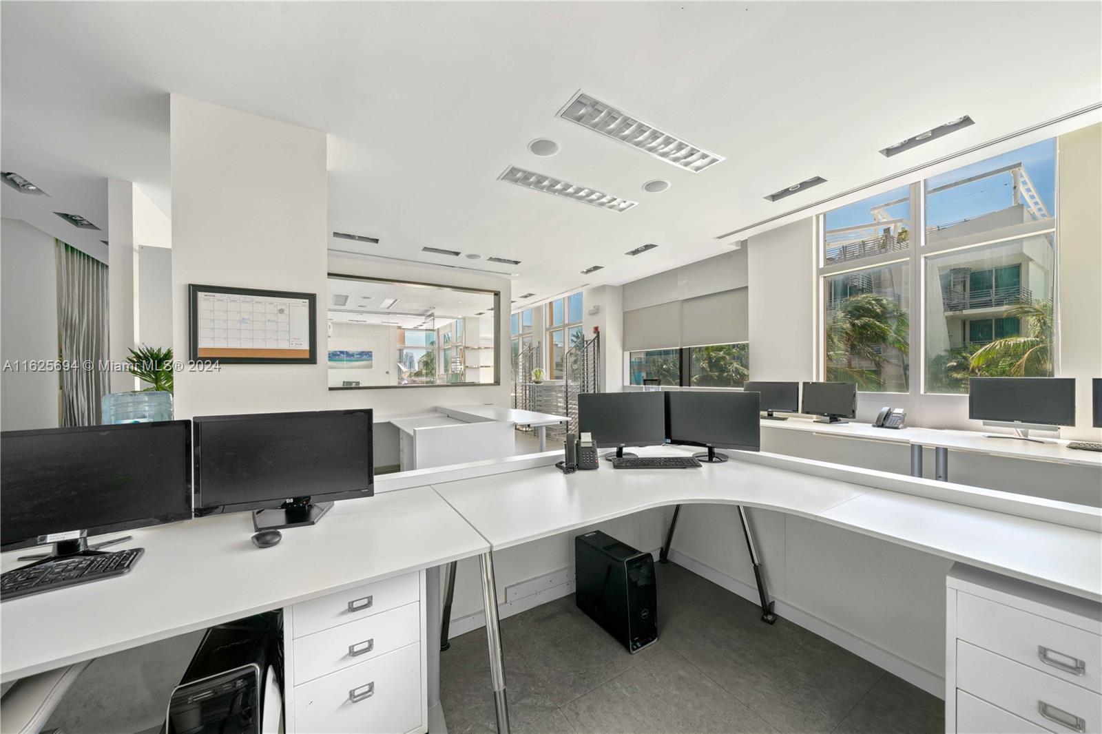 A modern office space features white corner desks, multiple computer monitors, and large windows — 1451 Ocean Dr # 204, Miami Beach FL 33139, MIAMI BEACH, FL