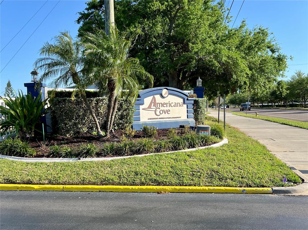 A sign for Americana Cove sits in a landscaped corner lot near a street — 7316 AMERICANA DRIVE NE UNIT 146, ST PETERSBURG, FL