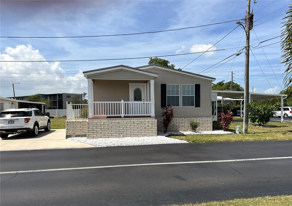 A single-story manufactured home features a front porch, tan siding, and a brick foundation — 7316 AMERICANA DRIVE NE UNIT 146, ST PETERSBURG, FL
