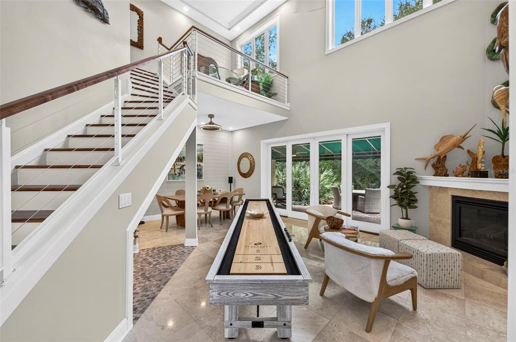 A living room features a shuffleboard table, staircase, fireplace, and large windows overlooking a patio — 4616 OAK HAMMOCK COURT UNIT 4616, PONCE INLET, FL
