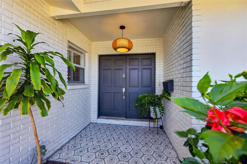 A covered entryway features a dark double door, white brick walls, and a patterned floor — 8450 FLAGSTONE DRIVE, TAMPA, FL
