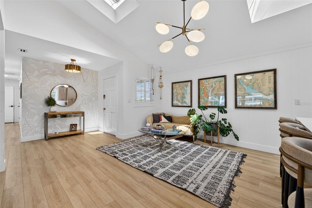 A bright living room features a vaulted ceiling, wood-look flooring, and a patterned area rug — 8450 FLAGSTONE DRIVE, TAMPA, FL