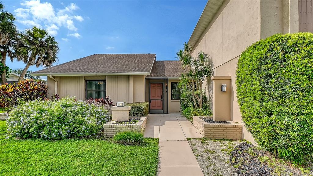 A tan house exterior features a front walkway, a red door, and landscaped green bushes — 3799 COUNTRYSIDE ROAD, SARASOTA, FL