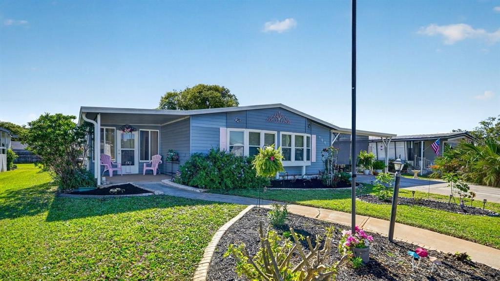 A blue single-story manufactured home features a covered porch, white trim, and landscaped front yard — 780 GREENFIELD DRIVE, PORT ORANGE, FL