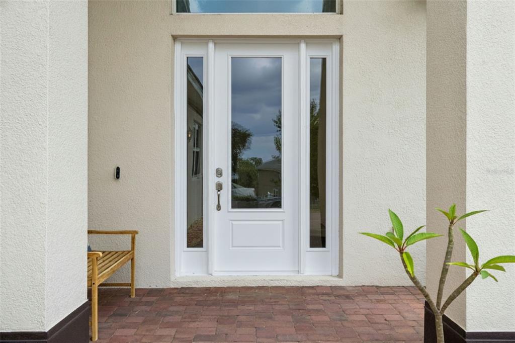 A white front door with glass panels and sidelights sits on a brick porch — 1837 MOORINGS COURT, CLERMONT, FL